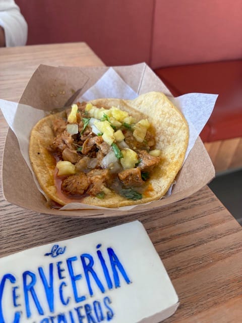 A taco sits in a paper tray on a brewery table.