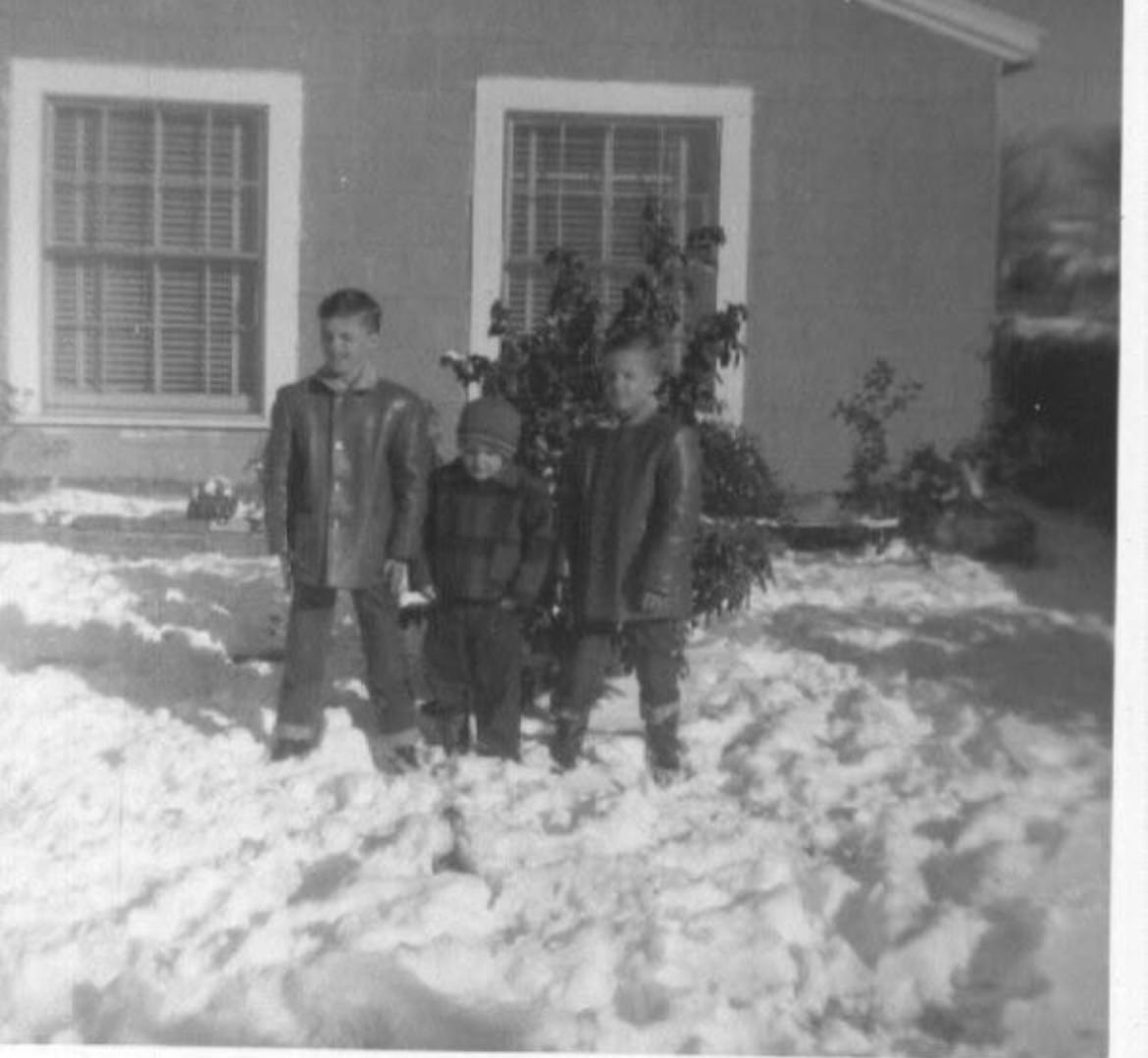 Old black and white photo of young boys standing in the snow in the front yard of a small house in the 1950s.