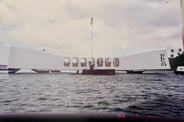 An old photo of the USS Arizona Memorial, a white marble structure over water.