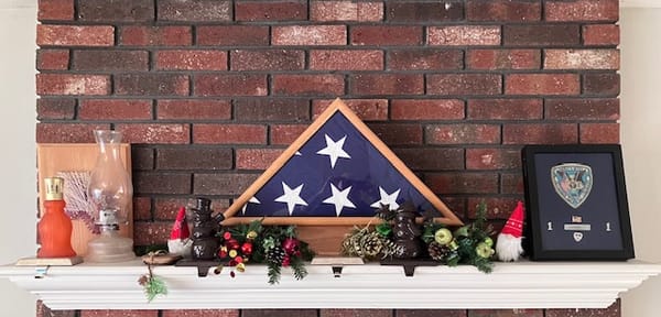 My father's American Flag folded and displayed in a light colored wood box on a white mantle.